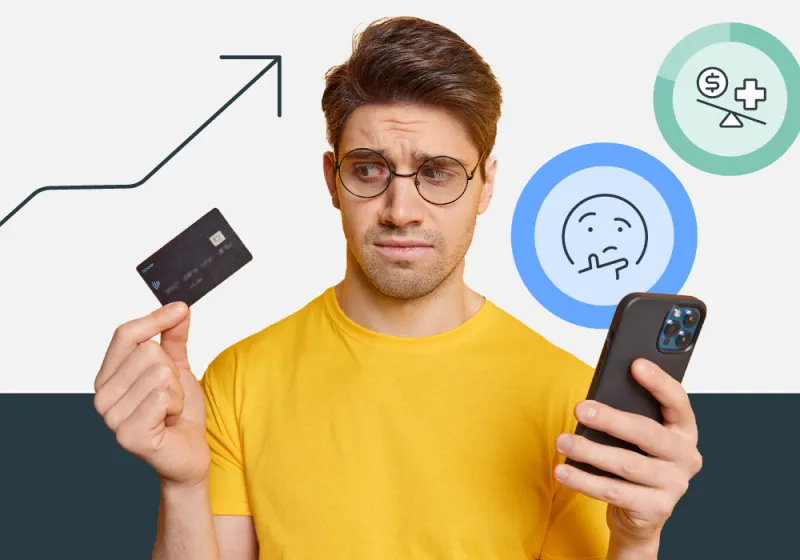 A  man in a yellow shirt, holding an Health Savings Account debit card in his right hand, and his phone in his left hand. He looks confused. 