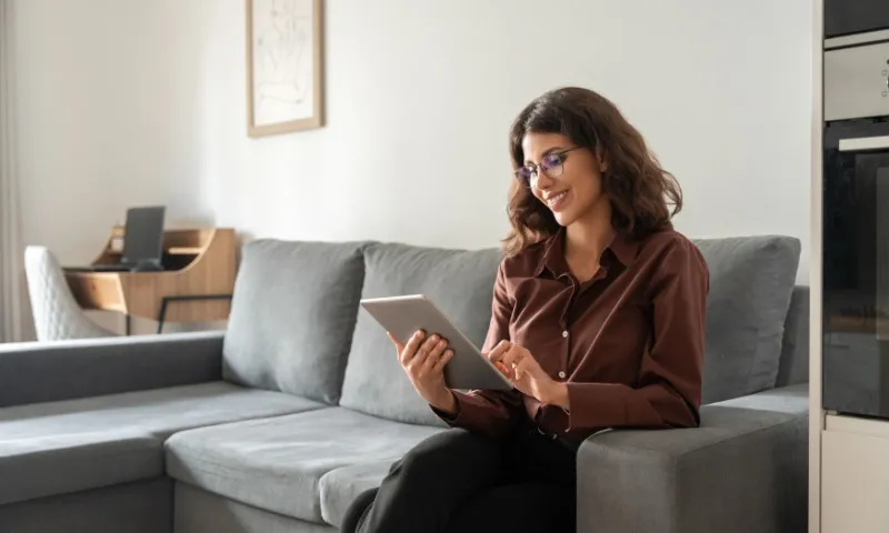 Businesswoman sitting on couch using tablet for working remotely.