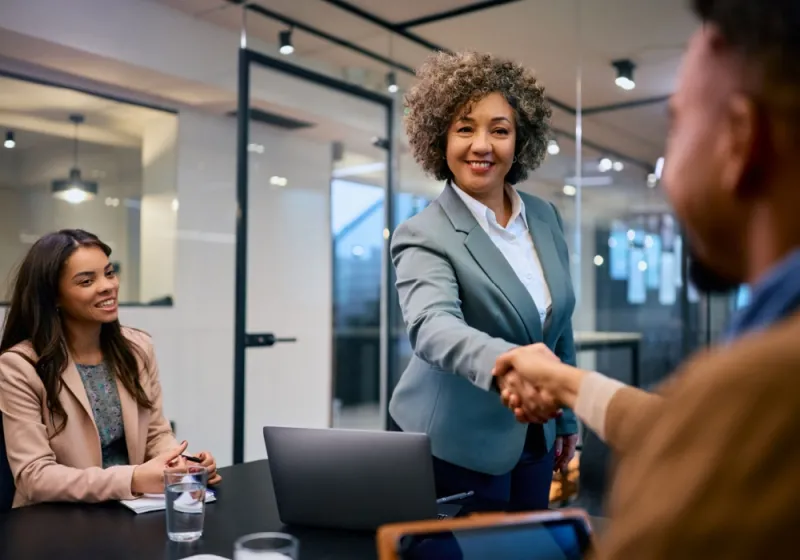 Happy CEO shaking hands with her colleague after successful business meeting in the office.