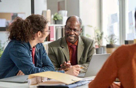Portrait of smiling senior man talking to young colleague in business meeting