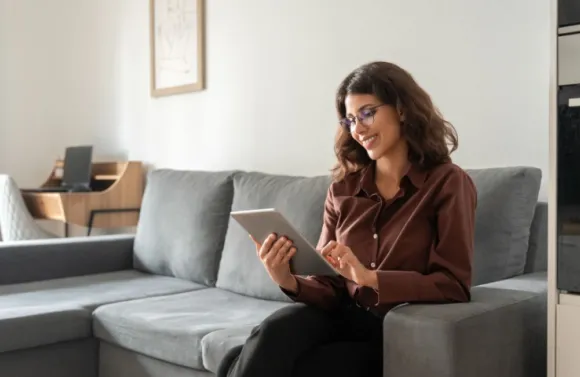 Businesswoman sitting on couch using tablet for working remotely.