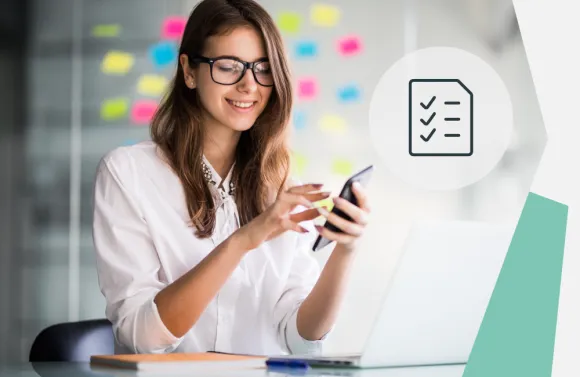 Person using a smartphone at a desk with a laptop, notebook, and pen; checklist icon overlay in view.