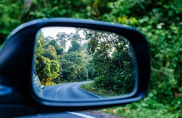 Car side mirror showing a winding road behind, symbolizing looking back over a past path