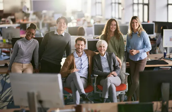 A multi-generational team of employees gathered in a modern office, representing collaboration, inclusion, and workplace connection.
