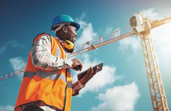 Field employee on a construction site uses a tablet while working outdoors, representing a dispersed workforce.