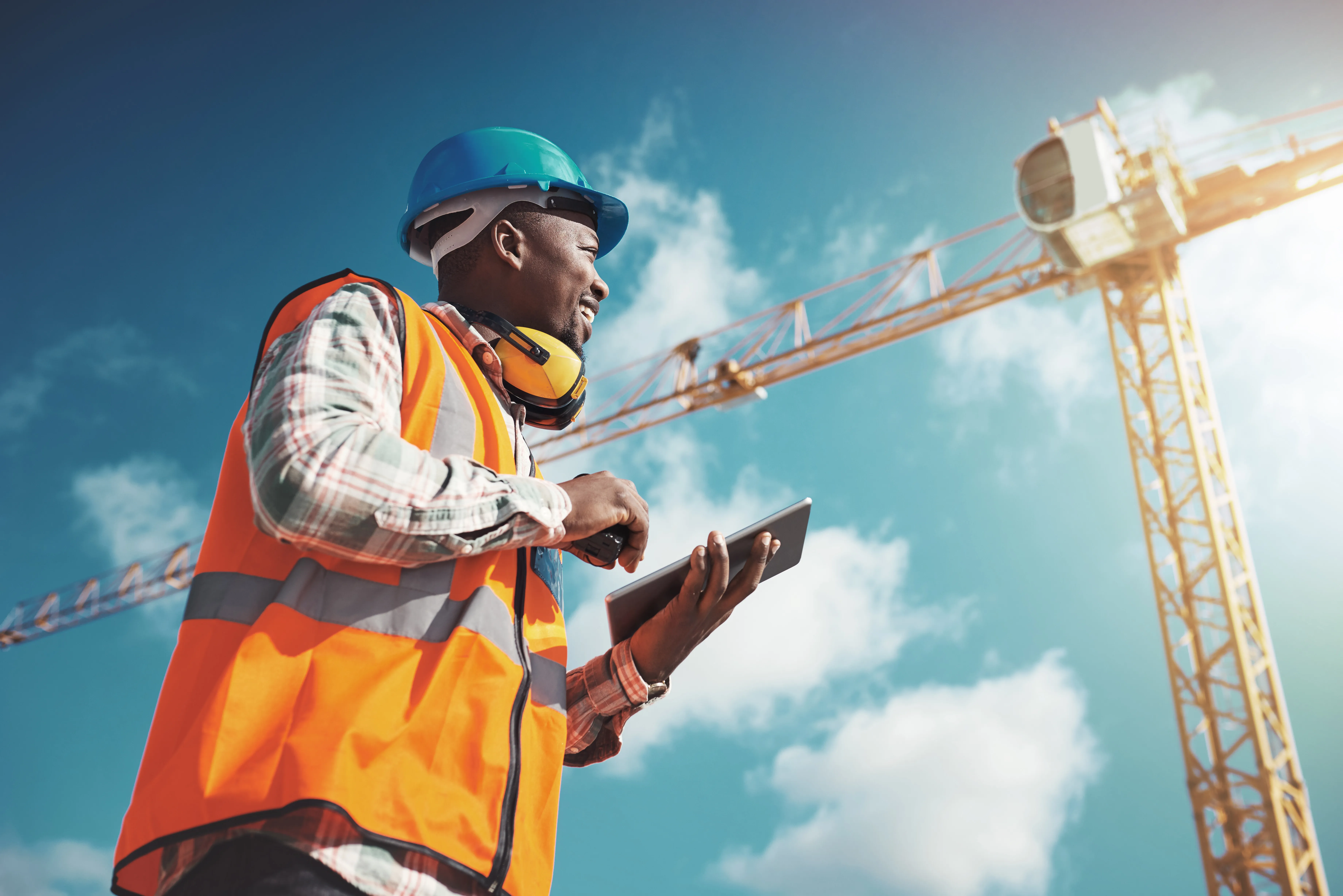 Field employee on a construction site uses a tablet while working outdoors, representing a dispersed workforce.