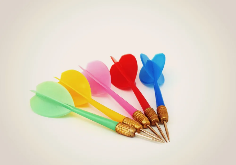 5 throwing darts grouped together. The darts are each a different color — one green, yellow, pink, red, blue.