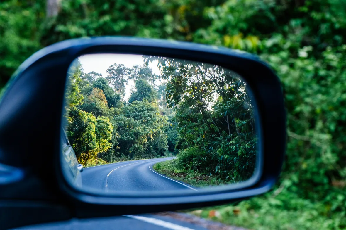 Car side mirror showing a winding road behind, symbolizing looking back over a past path