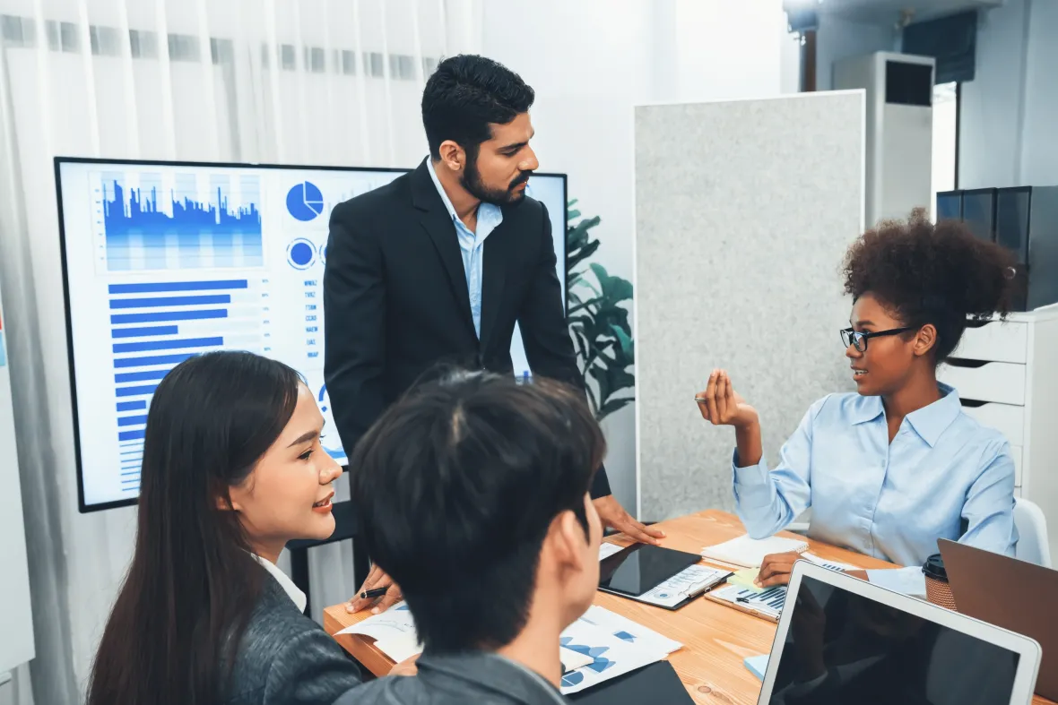 Business team reviews charts on a screen while discussing data-driven benefits strategy in a meeting.